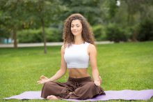 Pretty woman doing yoga exercises in outdoor park, green grass background