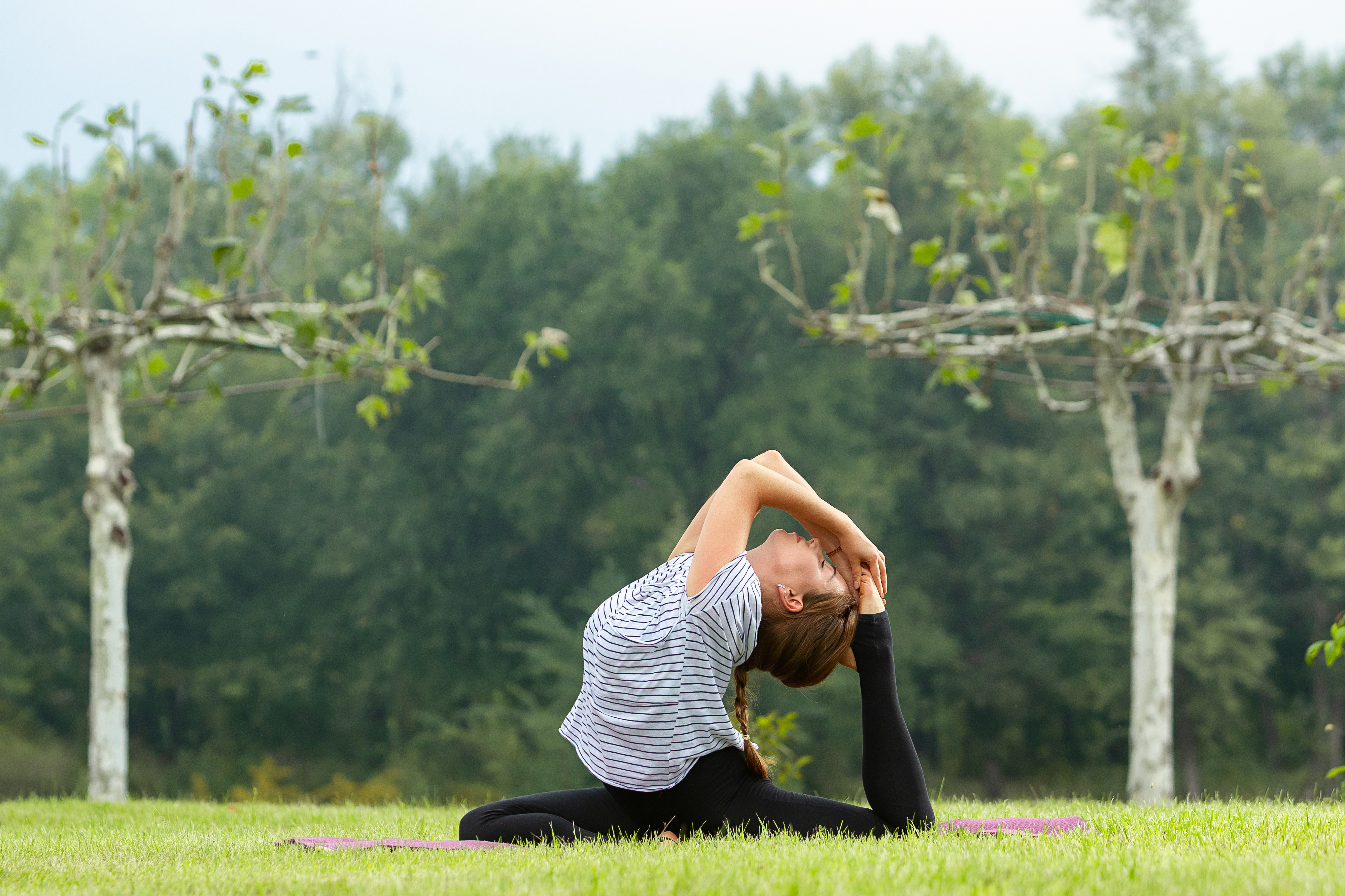 Young beautiful woman doing yoga exercise in green park. Healthy lifestyle and fitness concept.